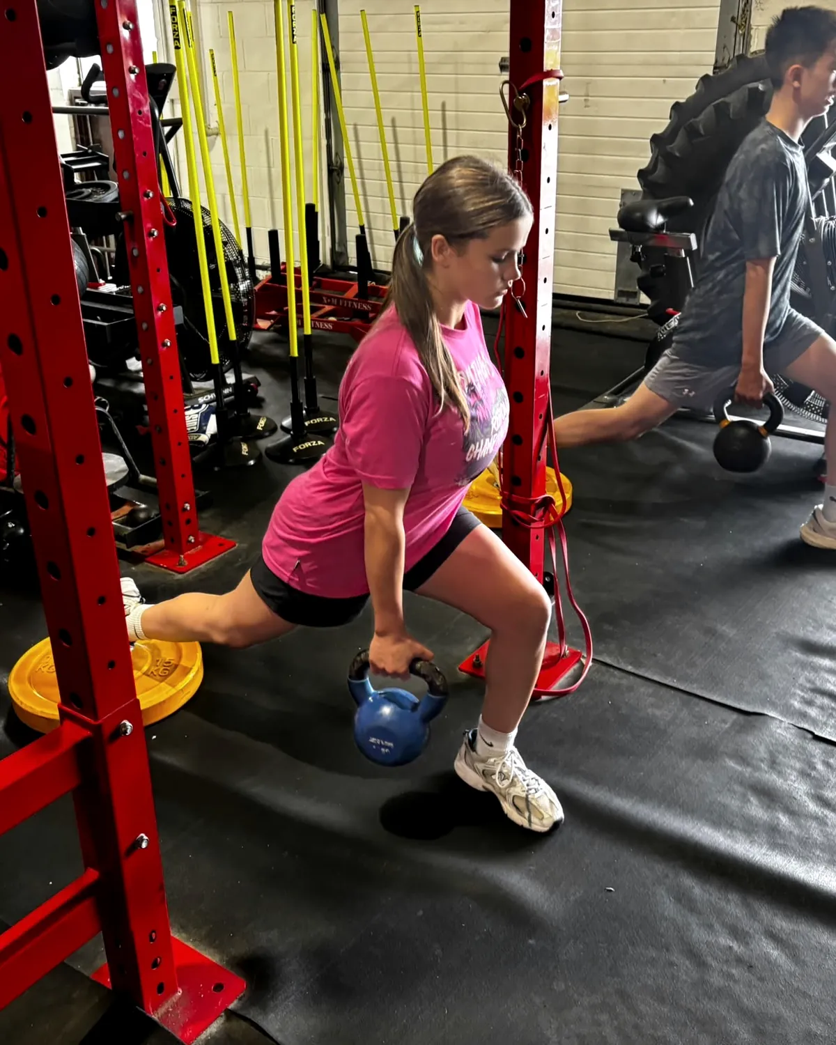 Two young athletes performing split squats with kettlebells